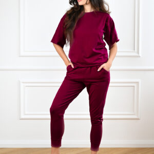 Bavlněné kalhoty a tričko Margaret v barvě burgundy na modelce s rukama v kapsách, přední pohled.